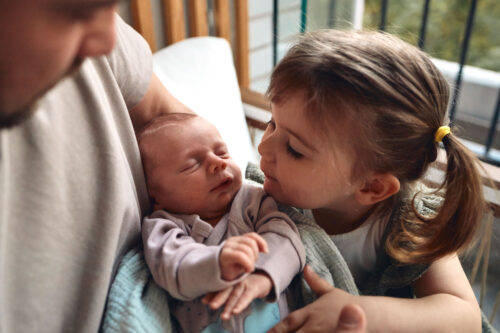 Father holding newborn baby while older sister is meeting him.